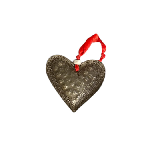 Handmade heart ornament with embossed pattern, red ribbon, and white bead, celebrating Haitian artisan craft.