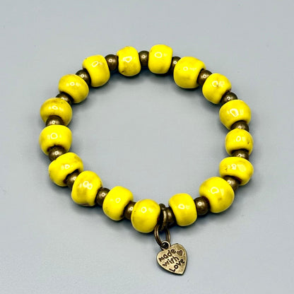 Vibrant yellow handmade bead bracelet with bronze spacers and 'Made with Love' heart charm, celebrating artisan craftsmanship.