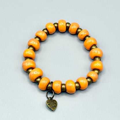 Handmade orange and bronze beaded bracelet with 'Made with Love' heart charm, celebrating artisan craftsmanship.
