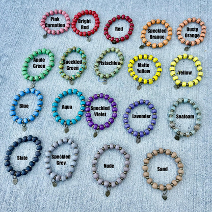 Handmade beaded bracelets in vibrant colors like pink, red, green, blue, purple, and neutral tones, each labeled with shade names.