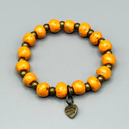 Handmade orange speckled bead bracelet with 'Made with Love' heart charm, celebrating artisan craftsmanship.