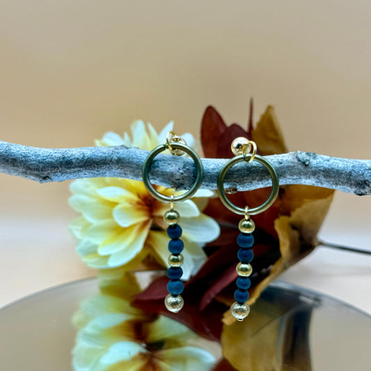 Handmade blue and gold beaded hoop earrings, artisan-crafted with cultural artistry, displayed on a branch with flowers.