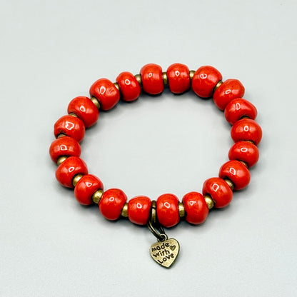 Vibrant red handmade bracelet with gold beads and 'Made with Love' heart charm, celebrating artisan craft.